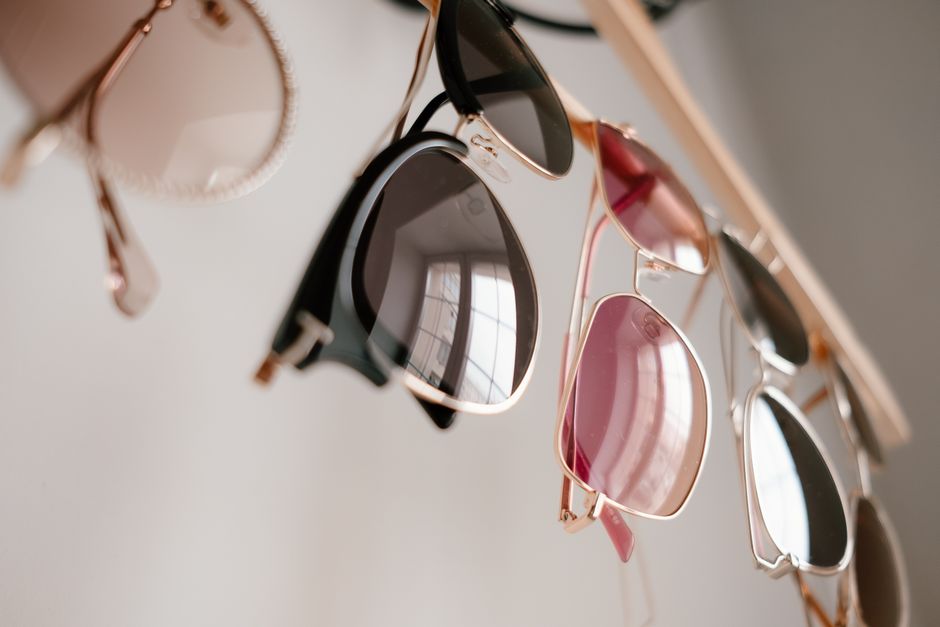 Stylish sunglasses in various colors hanging indoors with soft reflections.