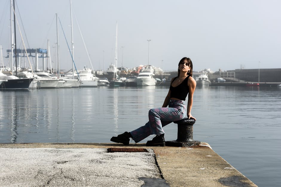 Young woman in a black crop top posing by yachts at a marina on a sunny day.