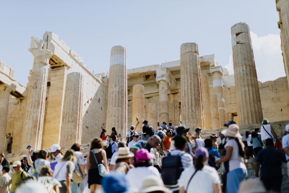 Crowds of tourists visiting the ancient Parthenon in Athens, Greece, under a clear blue sky.