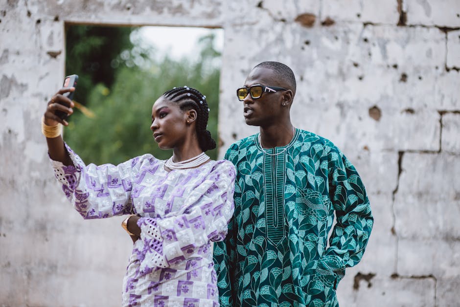 African couple in colorful traditional clothing capturing a selfie in an outdoor setting, highlighting cultural fashion.