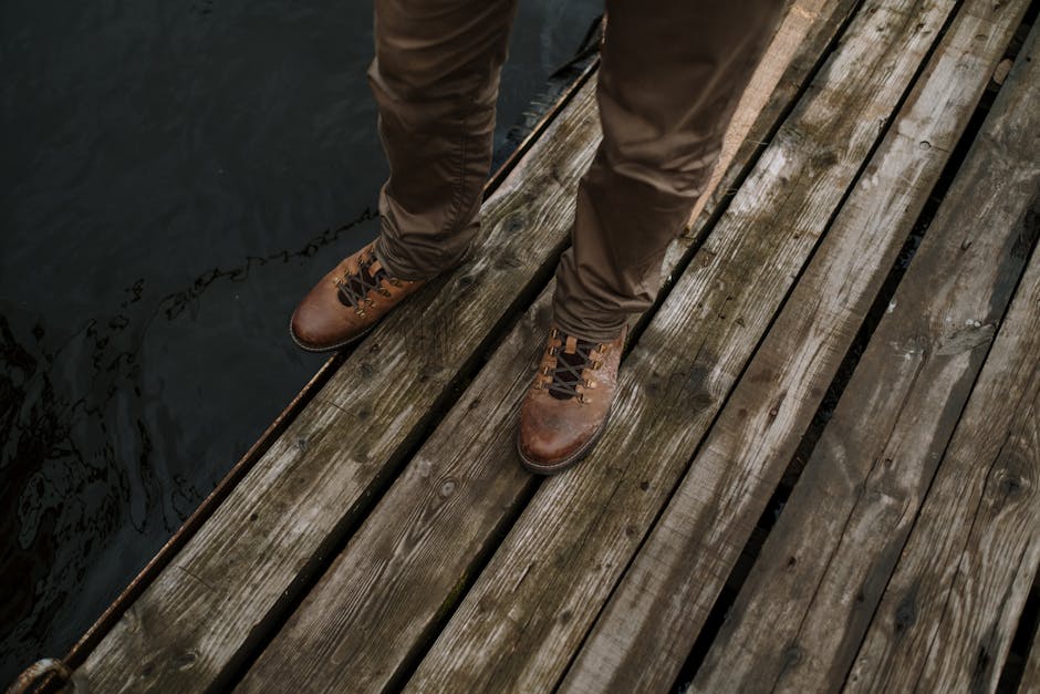 Close-up of brown leather boots and pants on a wooden dock by the water.