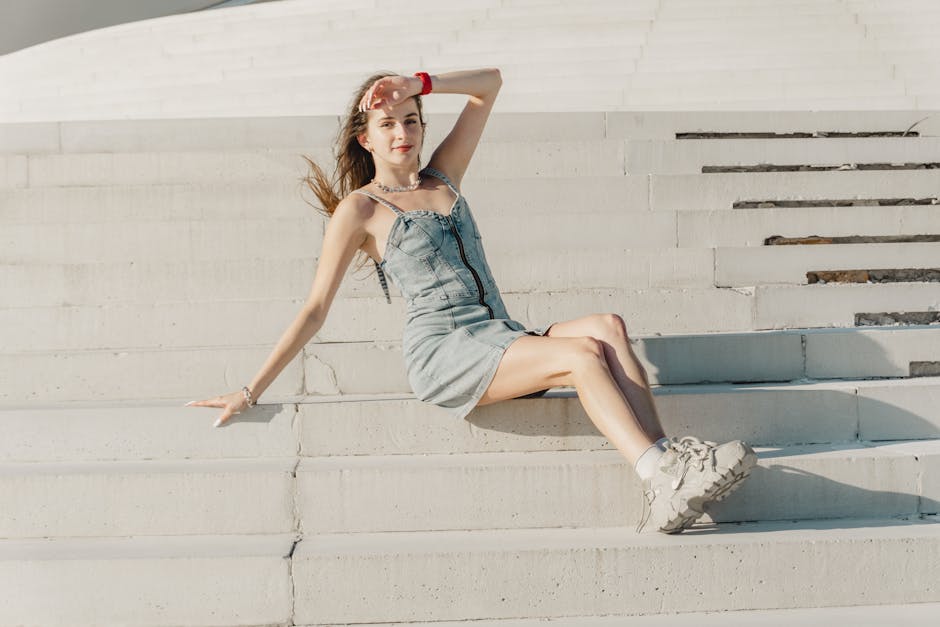 Woman in a denim dress sitting on sunlit stairs, exuding summer fashion vibes.
