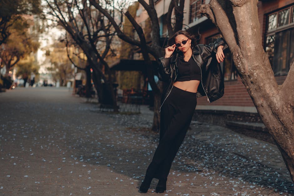 Stylish woman in black outfit poses in an urban autumn scene with scattered leaves.