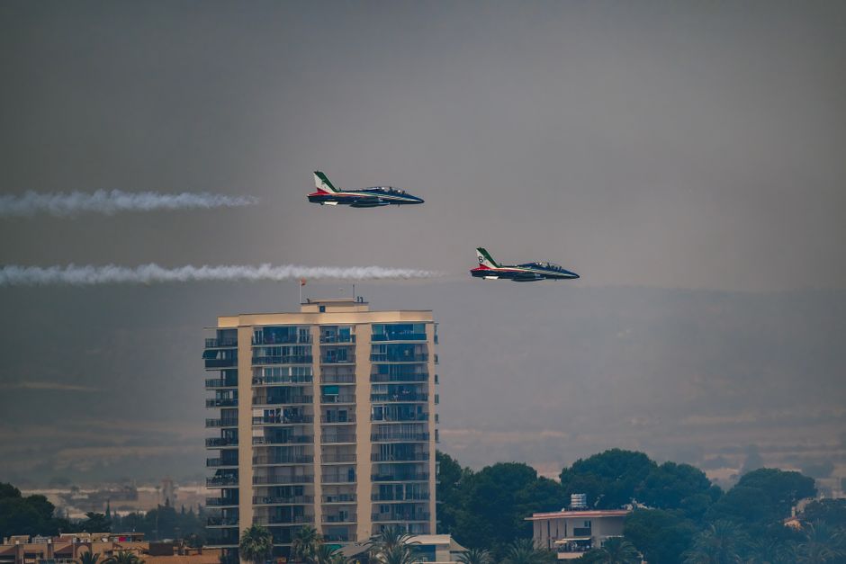 Two aerobatic jets fly in formation over a building in San Javier, showcasing precision and skill.
