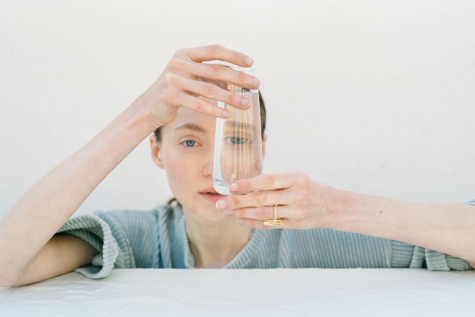 Portrait of a woman holding a glass of water, emphasizing reflection and minimalism.