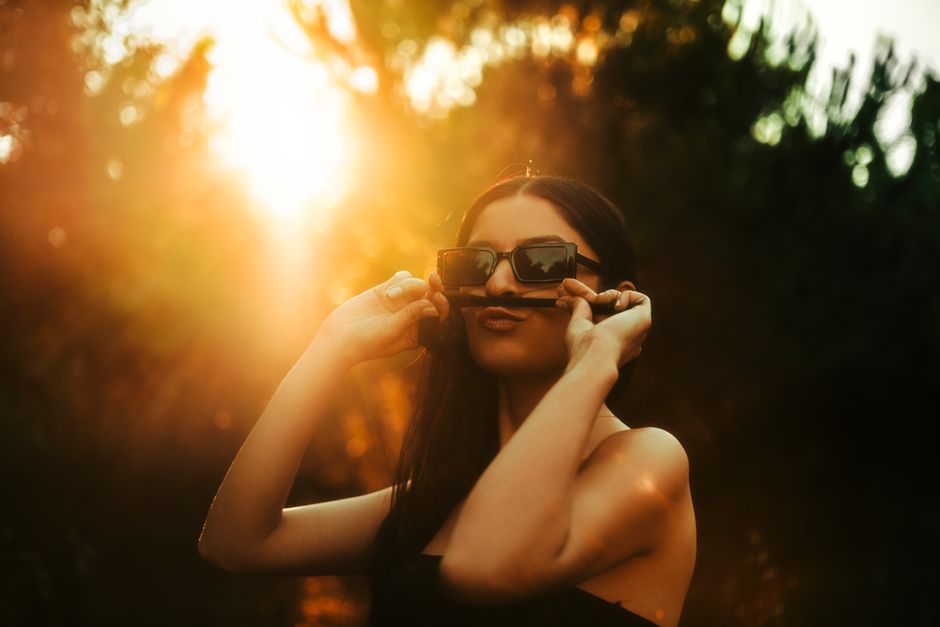 A young woman with sunglasses, making a mustache with her hair in sunlight.
