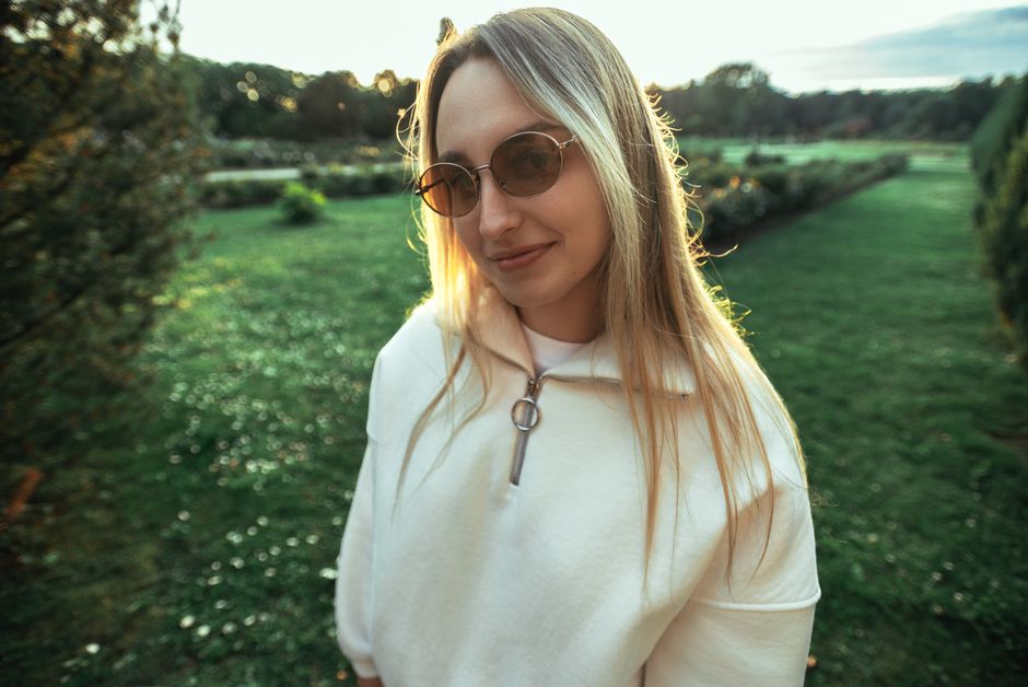 Woman in sunglasses and hoodie enjoying a sunny day outdoors with a park background.