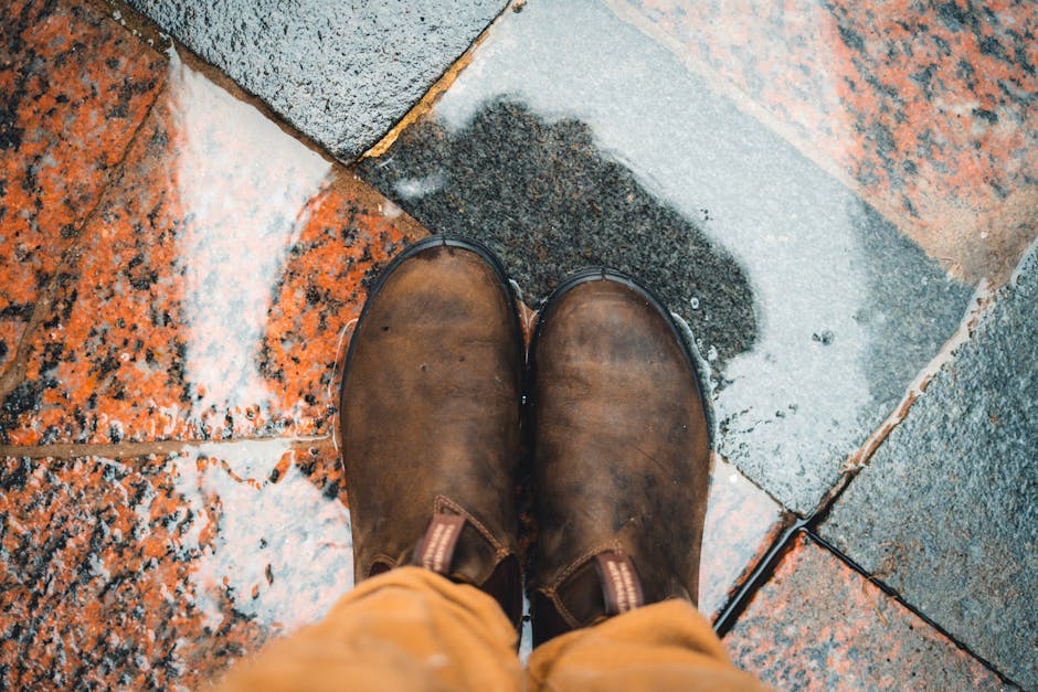 Brown leather boots standing on a wet pavement with colorful tiles and visible water reflections.