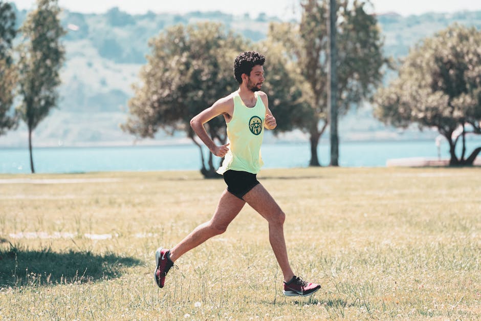 Side view of young determined male athlete in sportswear running on lawn in park near lake in sunny morning