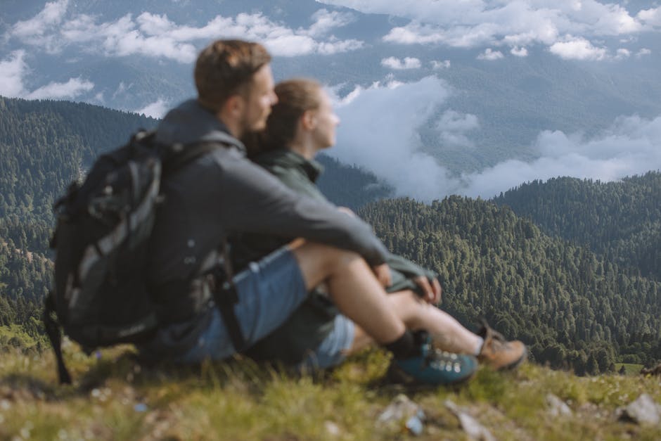 A couple of hikers sitting and enjoying a breathtaking mountain landscape view.