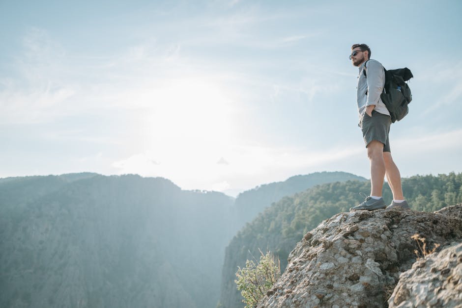 Man standing on a rocky mountain peak, gazing at scenic views under clear skies.