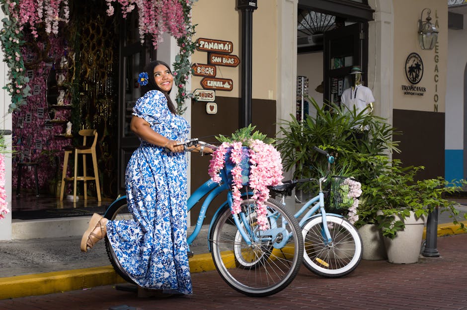 A woman in a floral dress poses with a decorated bicycle on a picturesque street in Panama City.