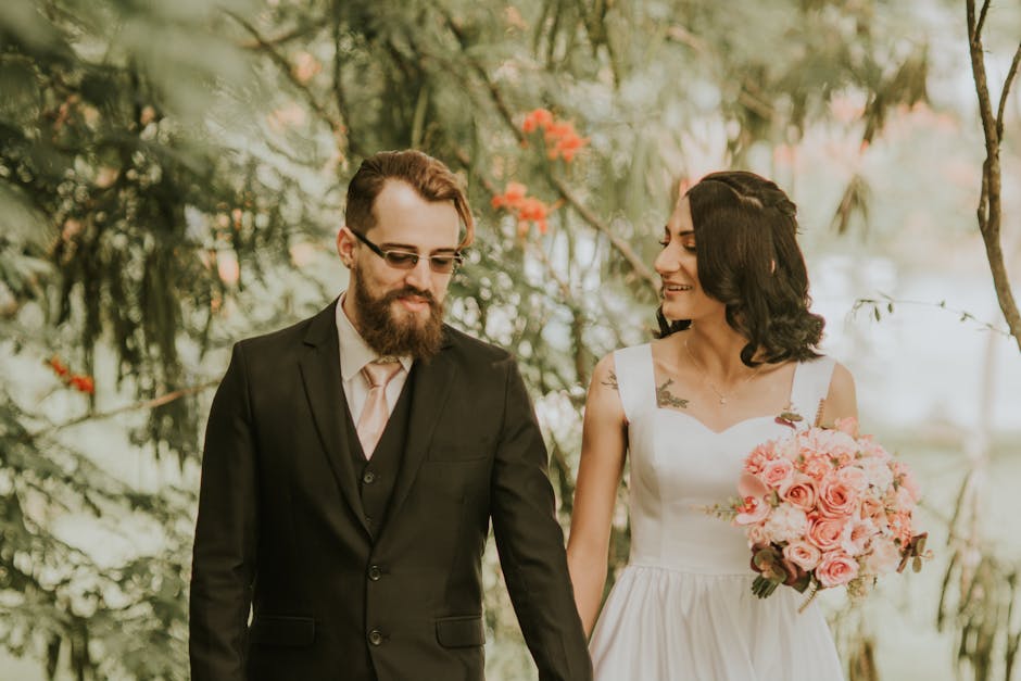 A newlywed couple smiles and walks together outdoors in a romantic setting.